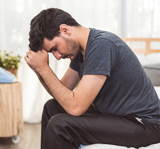 Man sitting with head bowed onto fists, looking somber